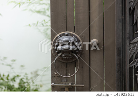 A close-up shot of a traditional bronze lion head door knocker attached to a dark wooden gate outdoors during the day A close-up shot of a traditional bronze lion head door knocker attached to a dark wooden gate outdoors during the day 143922613