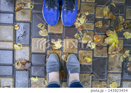 Two pairs of shoes on wet paved pavement with autumn leaves after rain Two pairs of shoes on wet paved pavement with autumn leaves after rain 143923454