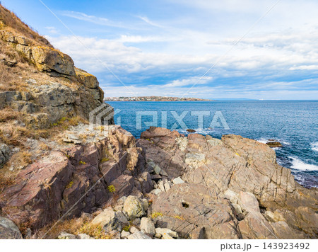 Rock shoreline beside blue water and distant land under a cloudy sky during daytime 143923492