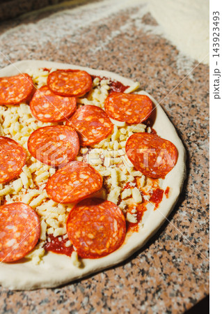 Unbaked pepperoni pizza topped with cheese and sauce rests on a kitchen counter Unbaked pepperoni pizza topped with cheese and sauce rests on a kitchen counter 143923493