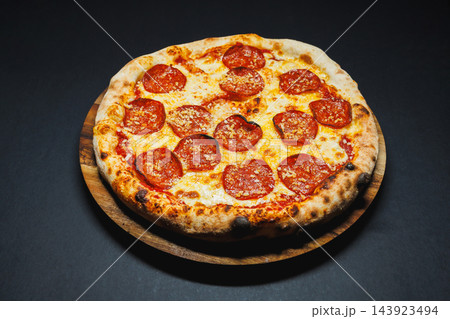 Pepperoni pizza with melted cheese served on a wooden board against a dark background 143923494