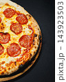 Pepperoni pizza with melted cheese on a wooden serving board against a dark background 143923503