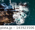 Waves break against a rocky coastline as seen from above during a daytime view of the sea 143923506