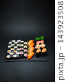 Sushi rolls, salmon nigiri, and shrimp pieces arranged on a black serving slate 143923508