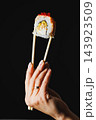 Hand holding sushi roll with chopsticks against a black background 143923509