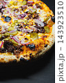 Close view of a baked pizza with cheese, meat, pickles, red onion, and a browned crust 143923510