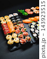 Assorted sushi and sashimi arranged on a black serving board for a meal 143923515