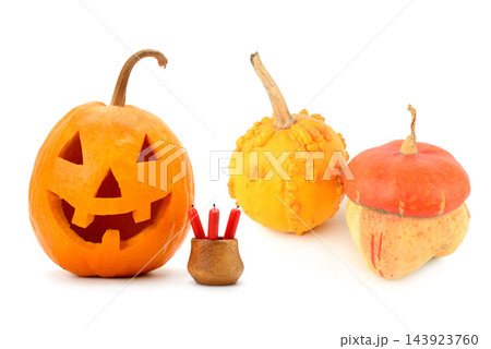 Horizontal view of carved Halloween jack-o-lantern pumpkin with decorative gourds and red candles isolated on white background 143923760