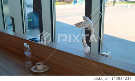 Coffee cup and water bottle sit beside a white gooseneck lamp on a wooden window counter. Bright modern setting represents comfort, convenience and a peaceful daytime break 143924237