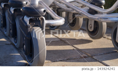 Close-up shows caster wheels and metal frames of parked mobility equipment on pavement. Wheelchair components represent accessibility, mobility assistance and practical support infrastructure 143924241