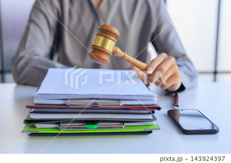 Attorney holding a wooden gavel above a pile of court paperwork on a workspace table. Attorney holding a wooden gavel above a pile of court paperwork on a workspace table. 143924397