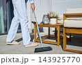 Person sweeping patio tiles with a long handled outdoor broom 143925770