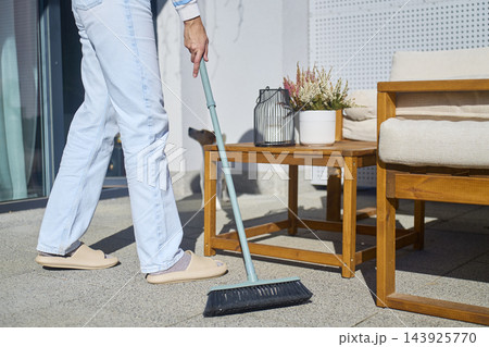 Person sweeping patio tiles with a long handled outdoor broom 143925770