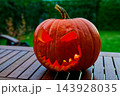 Spooky Halloween mood, glowing carved jack-o'-lantern with toothy grin on wooden table in dim lights 143928035