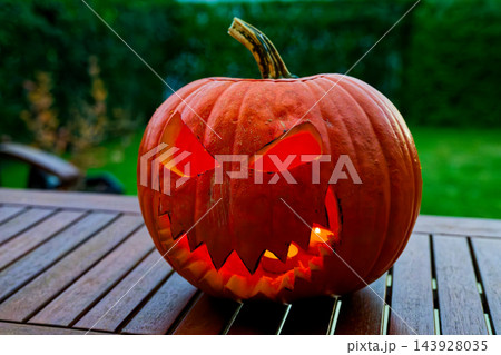 Spooky Halloween mood, glowing carved jack-o'-lantern with toothy grin on wooden table in dim lights 143928035