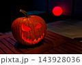 Spooky Halloween mood, glowing carved jack-o'-lantern with toothy grin on wooden table in dark lights 143928036