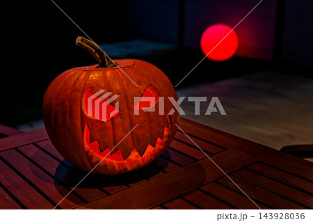 Spooky Halloween mood, glowing carved jack-o'-lantern with toothy grin on wooden table in dark lights Spooky Halloween mood, glowing carved jack-o'-lantern with toothy grin on wooden table in dark lights 143928036