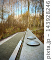 Metal footbridge with circular plates through a leafless woodland landscape 143928246