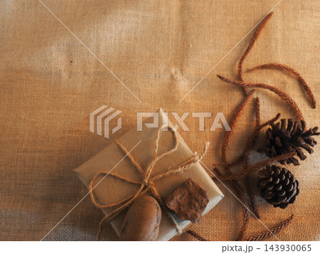 Eco-friendly gift box wrapped in craft paper with pine cones on rustic burlap background Eco-friendly gift box wrapped in craft paper with pine cones on rustic burlap background 143930065