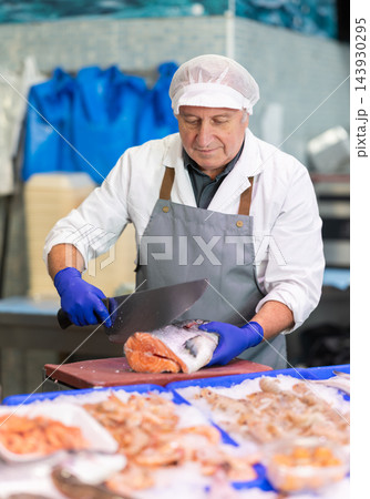 Senior fishmonger cutting fresh salmon fillet with large knife 143930295