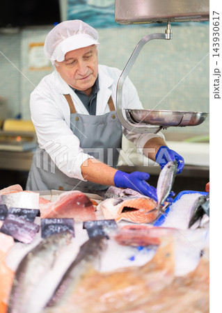 Mature salesman working behind fish market counter Mature salesman working behind fish market counter 143930617