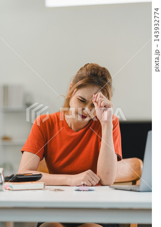 Stressed Asian woman touching forehead while managing financial problems with bills and calculator Stressed Asian woman touching forehead while managing financial problems with bills and calculator 143932774