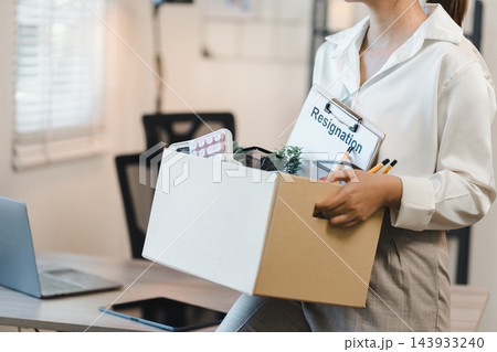 Woman holding box of office items with resignation clipboard and calm expression leaving workplace Woman holding box of office items with resignation clipboard and calm expression leaving workplace 143933240