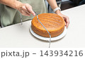 Woman cutting piece of sponge cake with knife on white plate in kitchen, homemade baking process, food preparation routine, cozy home cooking lifestyle. 143934216