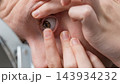 Person inserting a contact lens into an eye while looking into a mirror during close up personal care 143934232