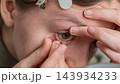 Person inserting a soft contact lens into a brown eye during close up eye care procedure 143934233
