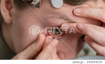Person inserting a soft contact lens into a brown eye during close up eye care procedure Person inserting a soft contact lens into a brown eye during close up eye care procedure 143934233