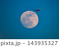 冬の本牧ふ頭から夕暮れの満月の前を夕焼けで朱色に輝き上昇するANA機が通過する姿を捉えた望遠風景 143935327