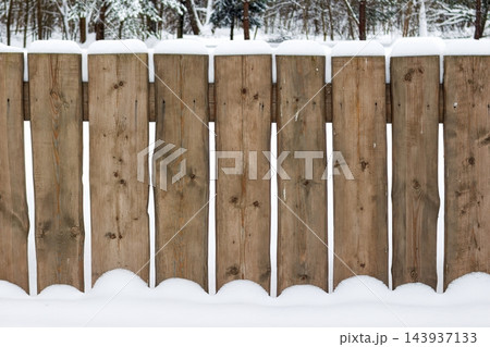 Weathered rustic wooden fence planks aligned in a row covered with fresh white winter snow against a blurred park background during a chilly frosty December day 143937133