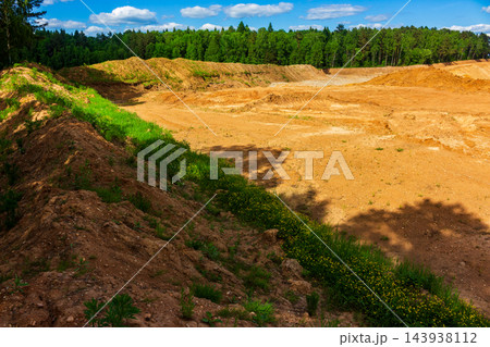 Scarred landscape of an open-pit sand quarry with massive earth mounds and piles of soil, cutting deep into the green forest line, dramatic evidence of industrial land transformation Scarred landscape of an open-pit sand quarry with massive earth mounds and piles of soil, cutting deep into the green forest line, dramatic evidence of industrial land transformation 143938112