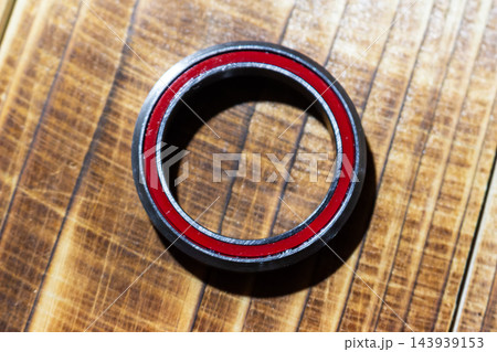Close-up of a high-quality bicycle headset cartridge bearing with red seals, resting on a textured wooden background 143939153