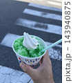 横断歩道を背景に手に持ったソフトクリームのせメロンかき氷 143940875