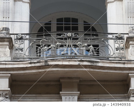 Vintage balcony with ornate black wrought iron railing on a light brick building facade. 143940938