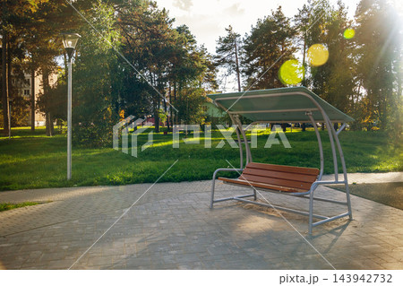 Sunlight shining on empty wooden swing bench with canopy in green public city park copy space 143942732