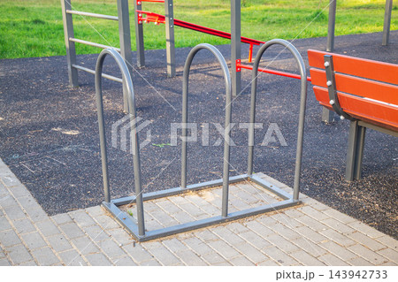 Empty metal bicycle rack in public park near outdoor playground and wooden bench 143942733