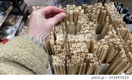 Customer hand selecting thin wooden craft sticks from assortment of natural wood strips displayed at hardware store Customer hand selecting thin wooden craft sticks from assortment of natural wood strips displayed at hardware store 143943939