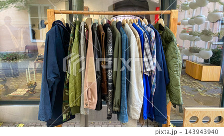 Assorted second hand jackets, coats and shirts hanging on wooden clothing rack at outdoor vintage clothing market 143943940