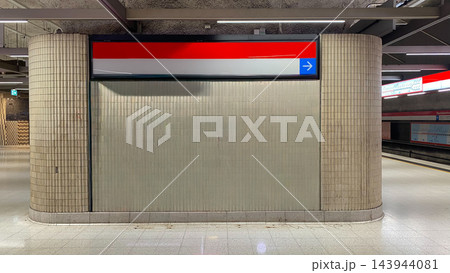 Large blank advertising display panel with red directional sign and blue arrow at empty underground metro station Large blank advertising display panel with red directional sign and blue arrow at empty underground metro station 143944081