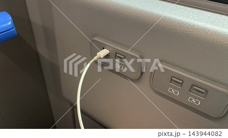 USB charging ports with connected white cable on the back of passenger seat in public transport vehicle 143944082