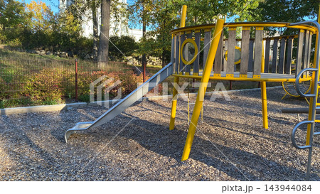 Empty outdoor playground with metal slide and yellow climbing structure on wood chip surface on sunny autumn day Empty outdoor playground with metal slide and yellow climbing structure on wood chip surface on sunny autumn day 143944084