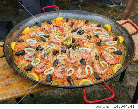 Giant Seafood Paella with Shrimp Mussels and Squid in Pan. Large seafood paella with shrimp, mussels, squid rings and lemon in large traditional pan. Spanish cuisine, outdoor food festival catering Giant Seafood Paella with Shrimp Mussels and Squid in Pan. Large seafood paella with shrimp, mussels, squid rings and lemon in large traditional pan. Spanish cuisine, outdoor food festival catering 143944241