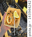 Portion of Seafood Paella with Squid and Lemon, takeaway food. Seafood paella with squid, green peas, lemon, disposable paper tray, held by hand. Spanish cuisine, street food, Outdoor Festival 143944242