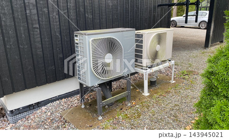 Outdoor heat pump units installed beside residential house for energy efficient heating and cooling system Outdoor heat pump units installed beside residential house for energy efficient heating and cooling system 143945021
