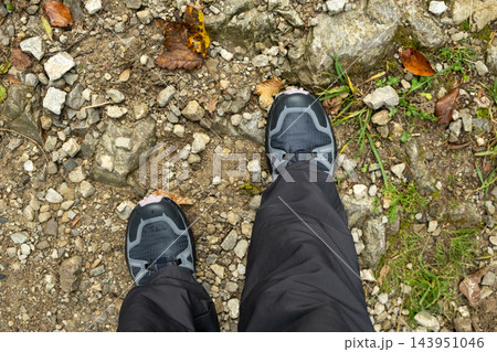 Hiking boots on forest trail covered with fallen leaves and stones 143951046