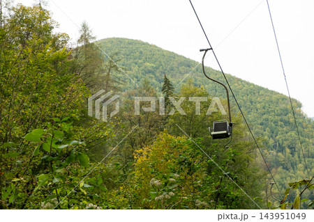 Single seat chairlift moving over mountain forest Single seat chairlift moving over mountain forest 143951049