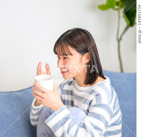 ソファでくつろぎながら飲み物を飲む若い女性 143951734